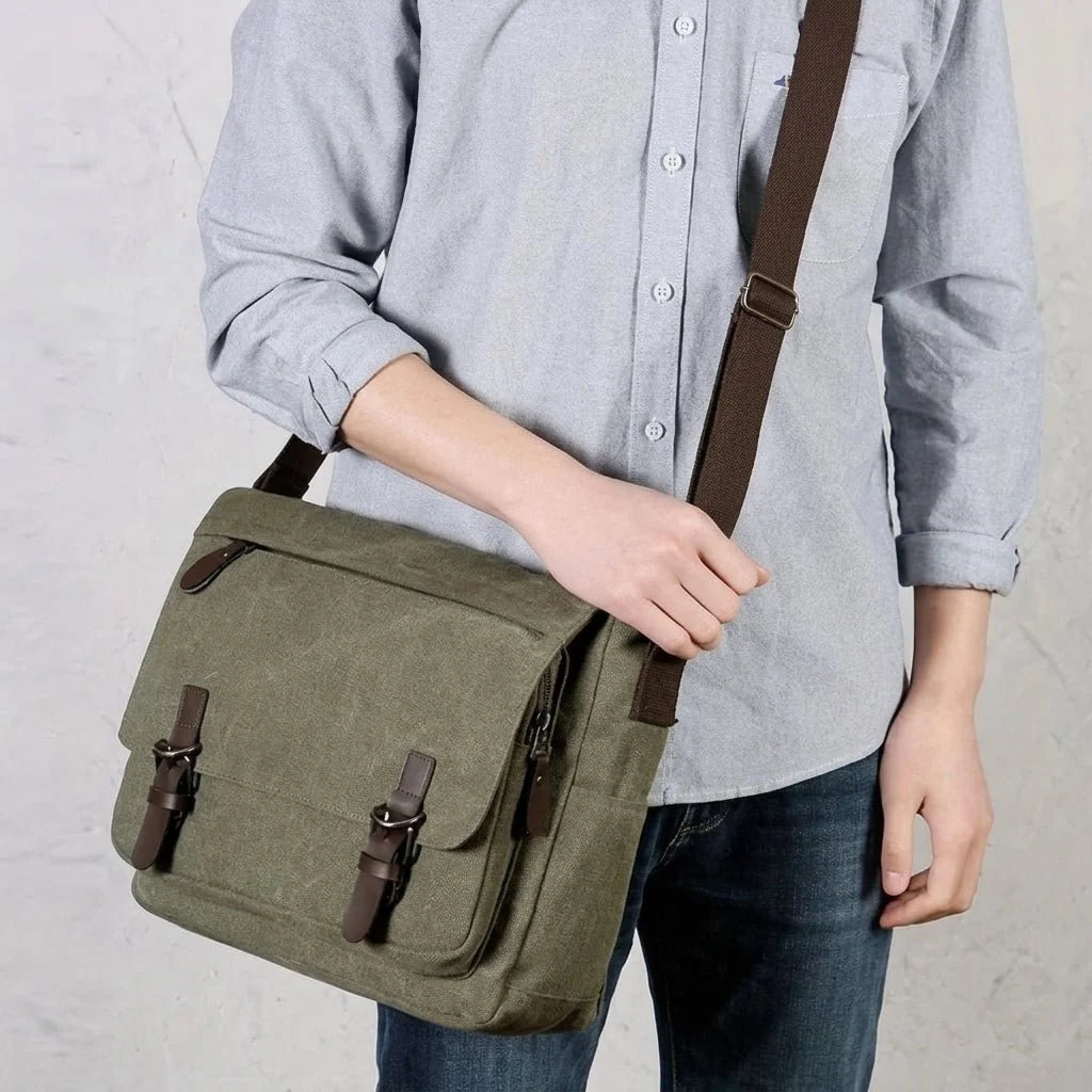 A person wearing a casual light blue shirt and jeans with a green canvas messenger bag featuring brown leather straps.