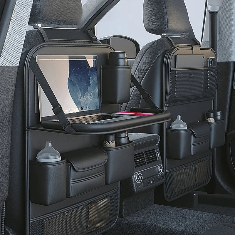 A black leather car seat organiser with a foldable tray holding a laptop, mounted on the back of a front car seat.