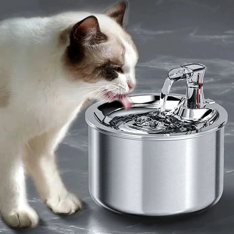 A white and brown cat drinking fresh water from a sleek, stainless steel pet fountain.