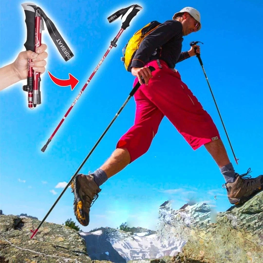 A hiker in red shorts and a yellow backpack uses foldable red trekking poles while climbing over rocky mountain terrain.