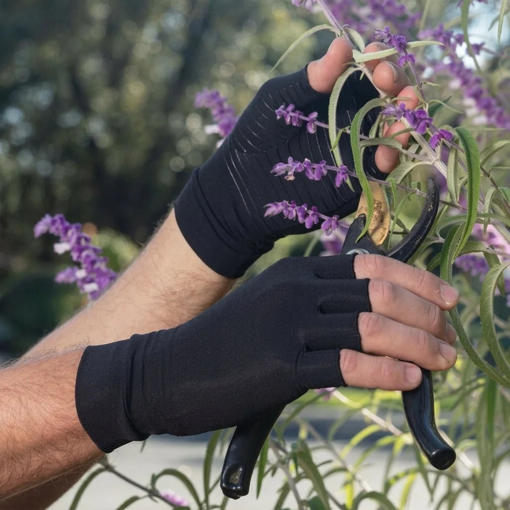 A person wearing black fingerless compression gloves while using garden shears to prune purple flowers.