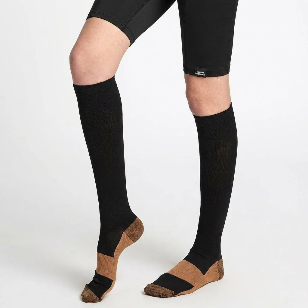 A person wearing black compression socks with copper-infused heels and toes, paired with black athletic shorts.