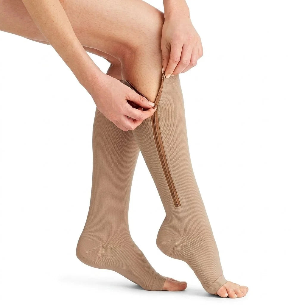 A person zipping up a pair of beige, open-toe compression socks on their lower legs.
