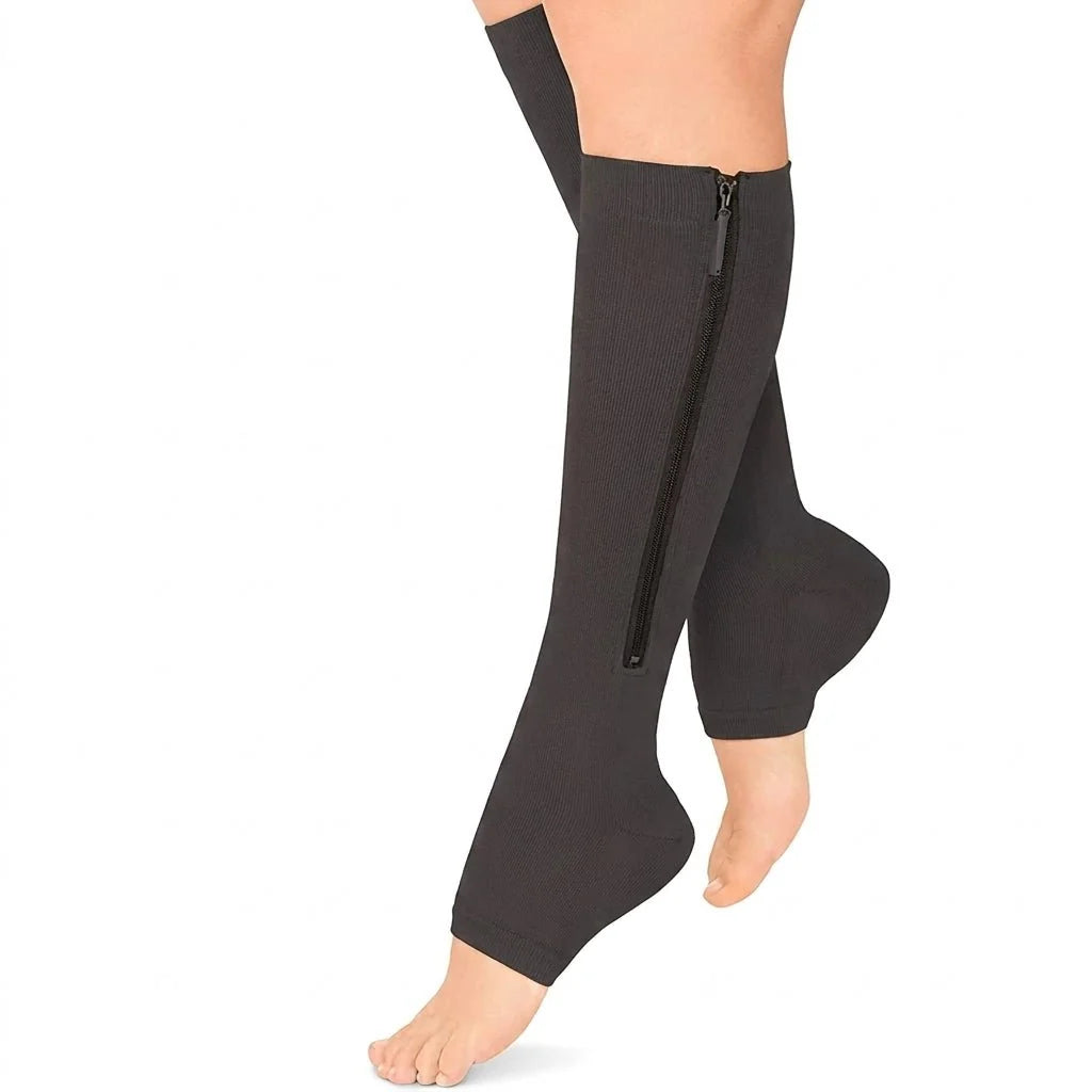 A pair of black, open-toe compression socks with a side zipper worn on a person's lower legs.