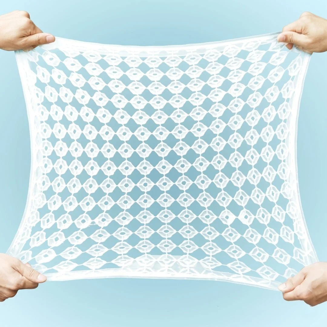 Two pairs of hands stretching a white, flexible, grid-patterned cooling gel car seat cushion against a light blue background.