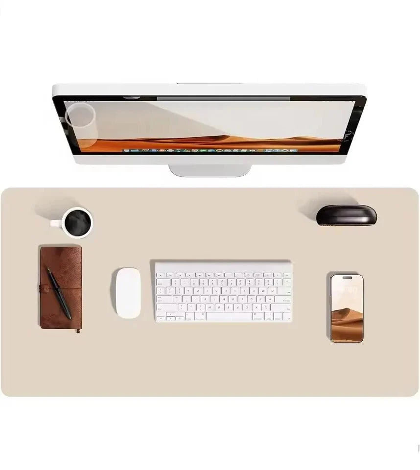 A minimalist desk setup featuring a large beige leather desk mat, a white computer, keyboard, mouse, phone, and a coffee cup.