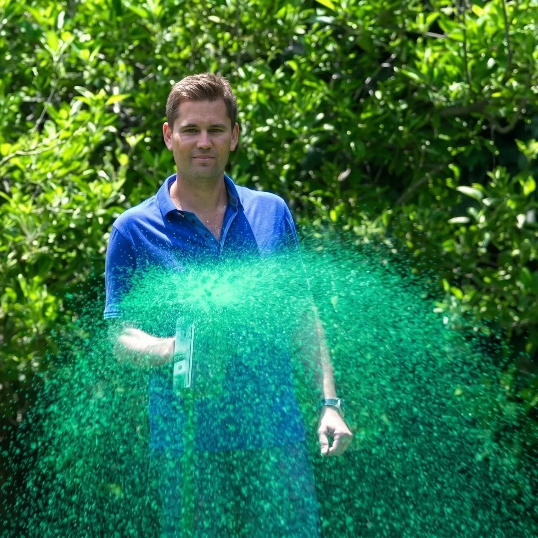 A man in a blue polo shirt spraying liquid grass seed from a handheld applicator in a lush green garden.