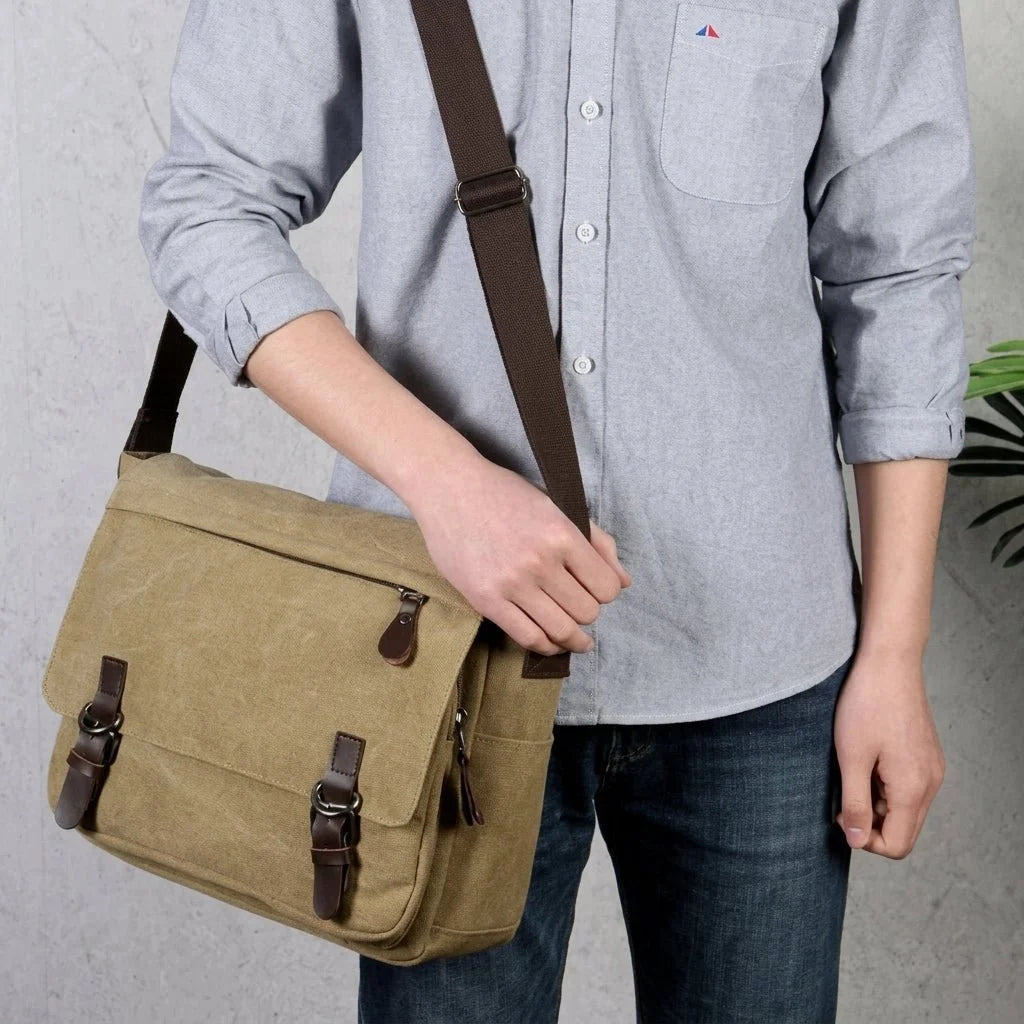 A person wearing a light blue shirt and dark jeans carries a tan canvas messenger bag with brown leather straps.