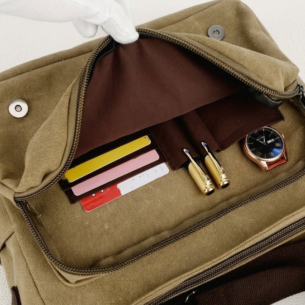 An open khaki canvas messenger bag showing internal pockets containing cards, two gold pens, and a wristwatch.