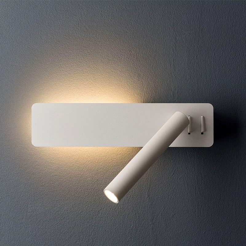A modern white wall sconce with a rectangular base and an adjustable cylindrical reading light, mounted on a dark wall.