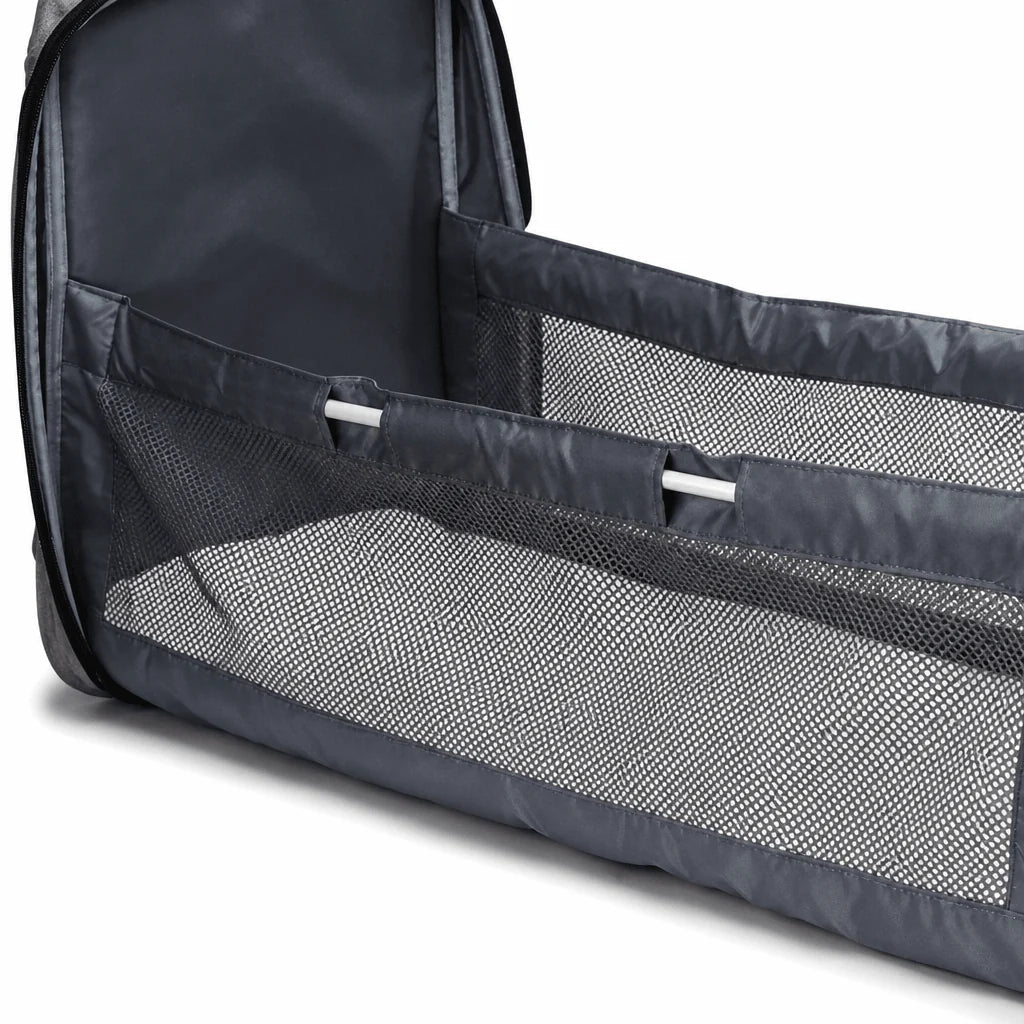 A close-up view of a grey portable baby travel cot with mesh sides and a soft mattress base.